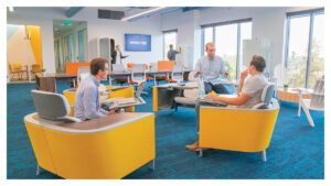 Photograph of group of men meeting in work space. Men sitting on yellow chairs collaborating and working together.
